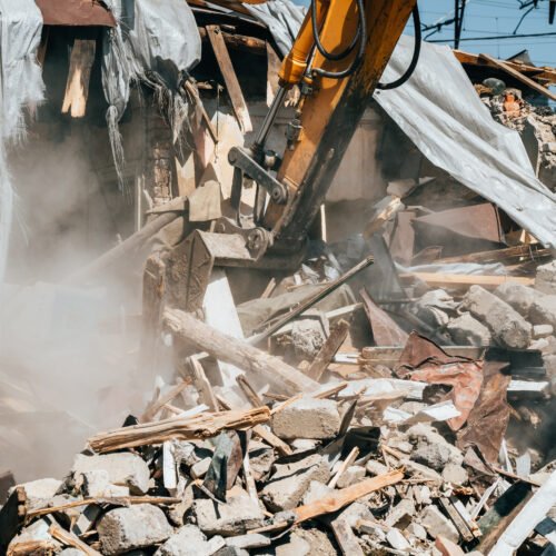 Destruction of old house by excavator. Bucket of excavator breaks concrete structure.