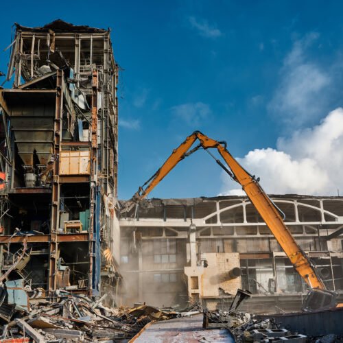 Demolition of a multi-storey tower of an industrial building. The operation of a high-altitude destroyer equipped with hydraulic shears. Winter sunny day.