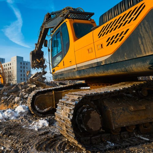 Bucket of crawler excavator at process of dismantling on construction site closeup. Destruction of old buildings. Gathering of concrete and metal reinforcement debris