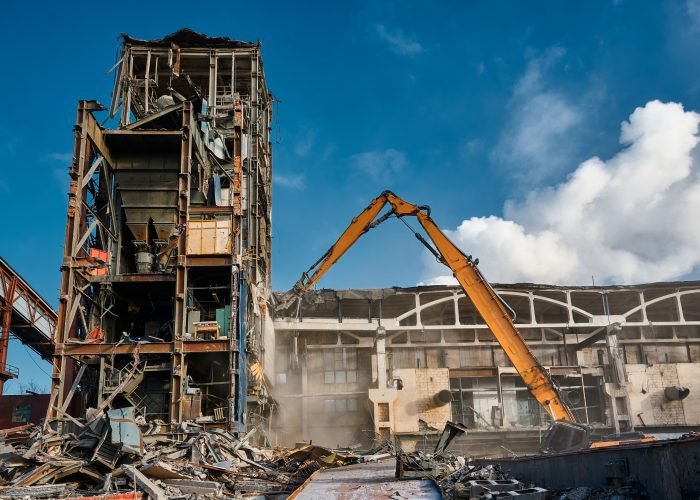Demolition of a multi-storey tower of an industrial building. The operation of a high-altitude destroyer equipped with hydraulic shears. Winter sunny day.